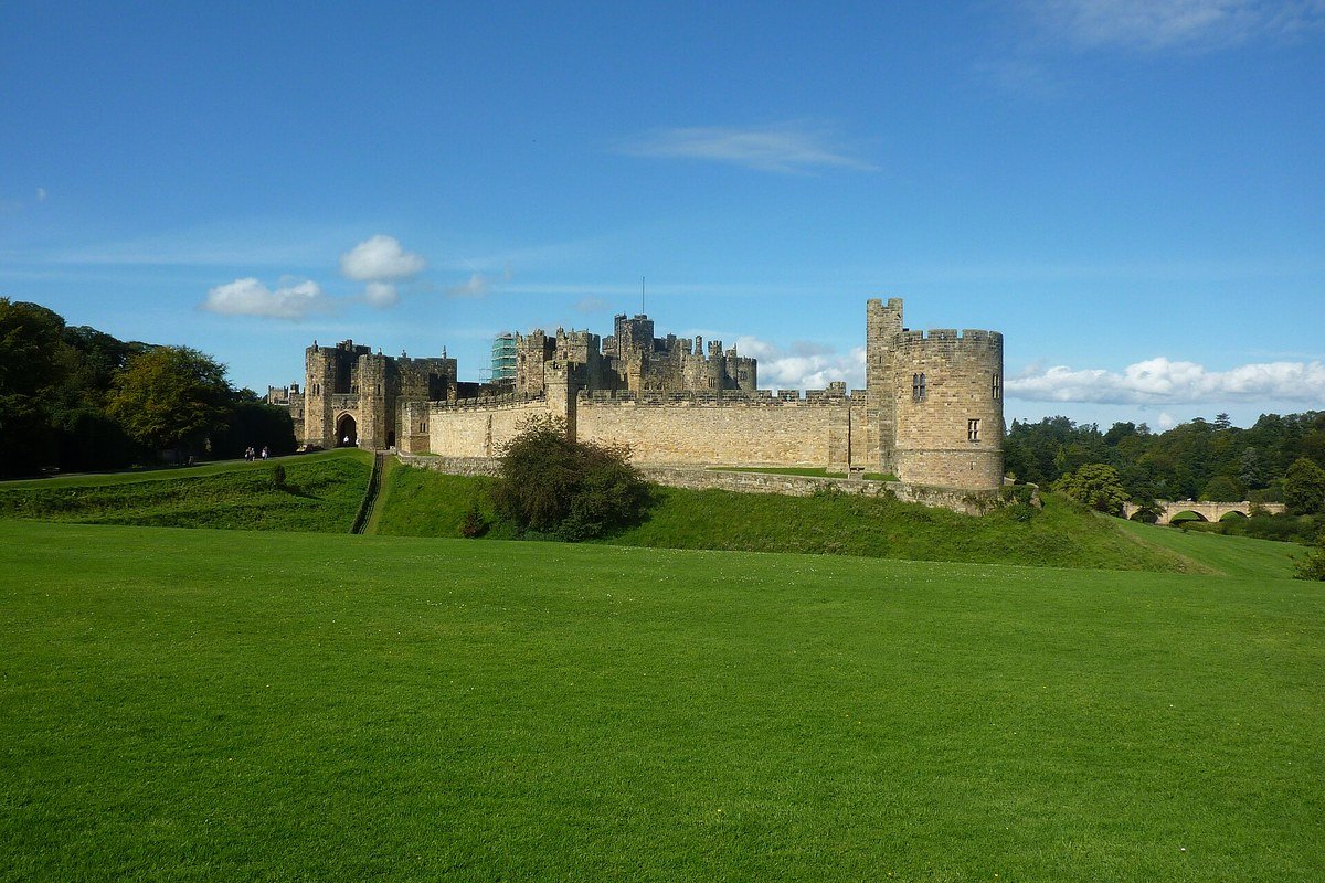 İngiltere'nin Northumberland bölgesindeki Alnwick Kalesi'nin geniş yeşil çimenlerin ardında yükselen taş surları ve kuleleri