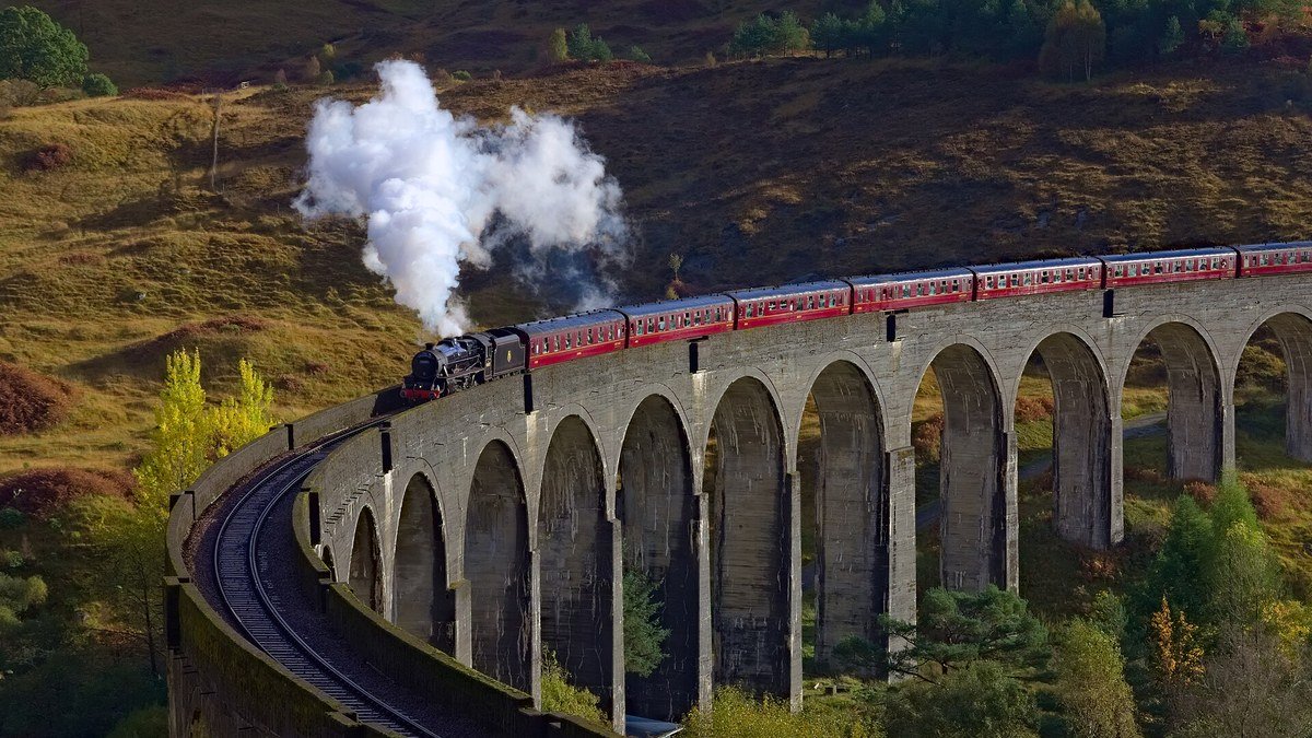 İskoçya'da sonbahar renklerine bürünmüş tepelerin arasında, kemerli Glenfinnan Viyadüğü'nün üstünden dumanlar çıkararak geçen kırmızı vagonlu buharlı tren