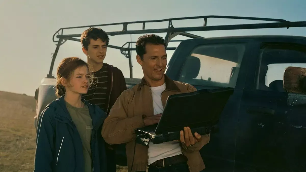 Interstellar filminden sahne: kamyonetin önünde elindeki dizüstü bilgisayara bakan Cooper, yanında kızı Murph ve oğlu Tom