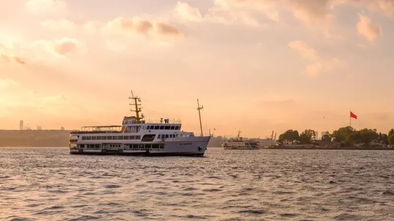 Gün batımında Boğaz’da ilerleyen beyaz bir İstanbul vapuru, turuncu gökyüzü ve sakin deniz