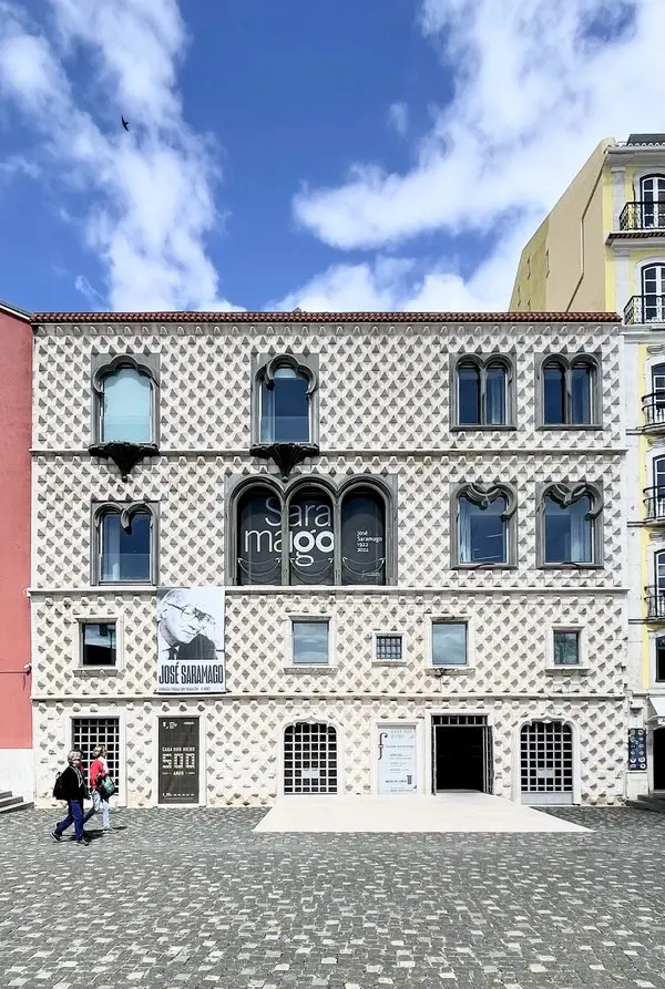 Lizbon’daki Casa dos Bicos binasının elmas biçimli taşlarla kaplı cephesi; pencerede Saramago yazısı, girişin yanında yazarın portresinin bulunduğu bir afiş