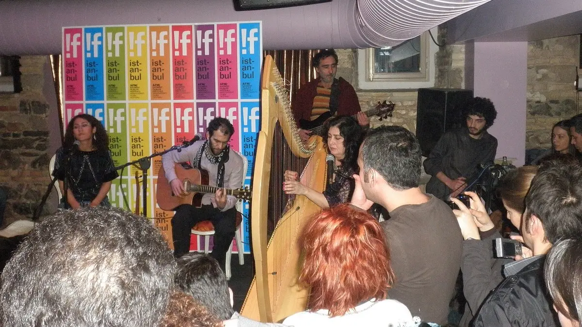 İstanbul’daki bir festival konserinde sahnede Kürtçe şarkılar seslendiren Aynur Doğan, gitarıyla Mehmet Atlı ve arp çalan Tara Jaff; önde onları dinleyen ve fotoğraf çeken seyirciler