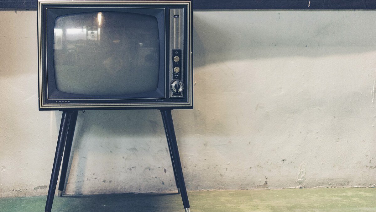 Beyaz bir duvarın önünde ince metal ayaklar üzerinde duran ahşap kasalı eski tüplü televizyon