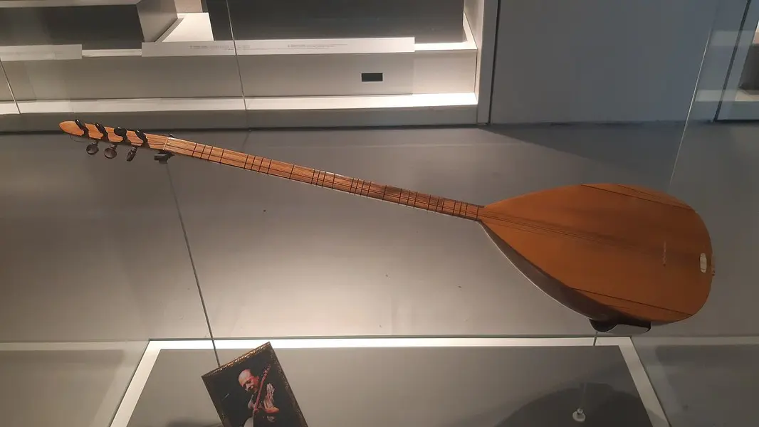 Cam vitrinde sergilenen, Neşet Ertaş’a ait uzun saplı ahşap bağlama; önünde ustanın bağlama çalarken çekilmiş küçük bir fotoğrafı