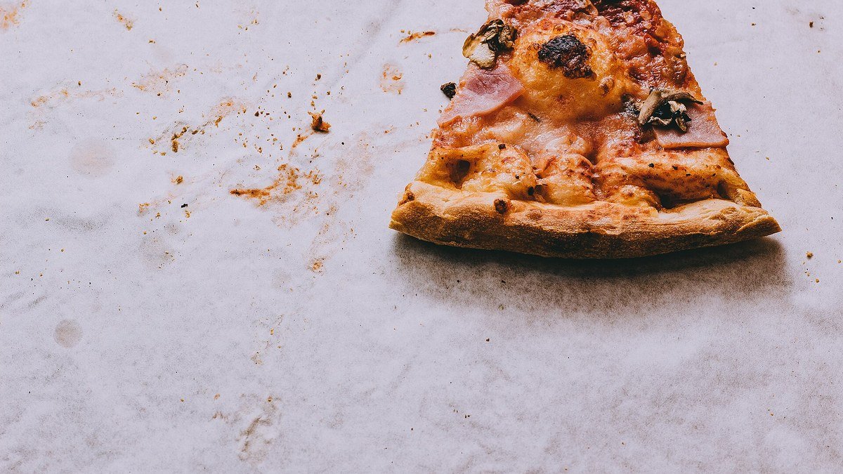 Beyaz bir masanın üstünde, etrafında kırıntılar bulunan son bir dilim pizza
