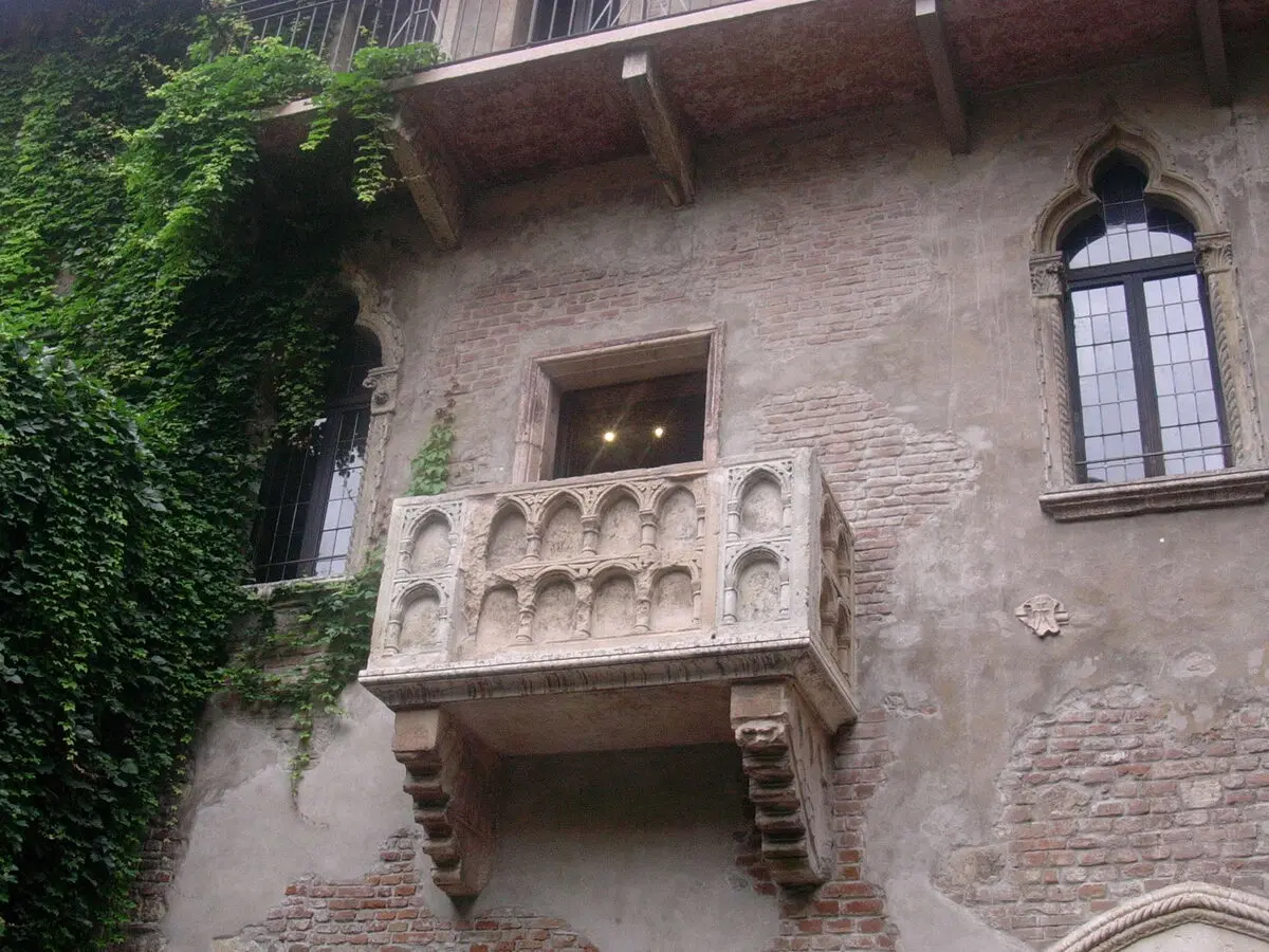 Verona’daki Juliet’in Evi’nin taş cephesinde, kemerli oymalarla süslü mermer balkon; solda duvarı kaplayan sarmaşıklar, sağda sivri kemerli bir pencere
