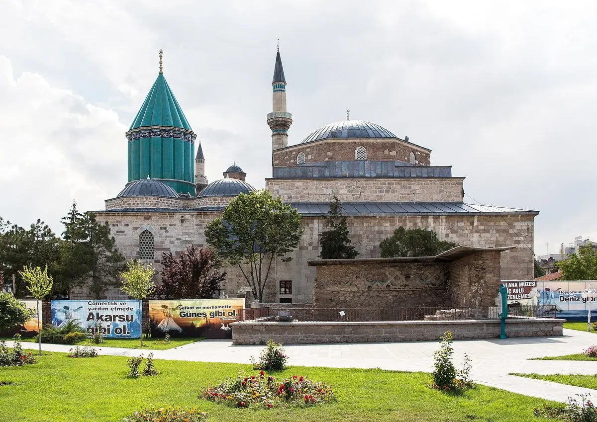 Konya’daki Mevlânâ Müzesi: yeşil çinili Kubbe-i Hadrâ, yanında kurşun kubbeli cami ve minare, önünde çiçekli bahçe