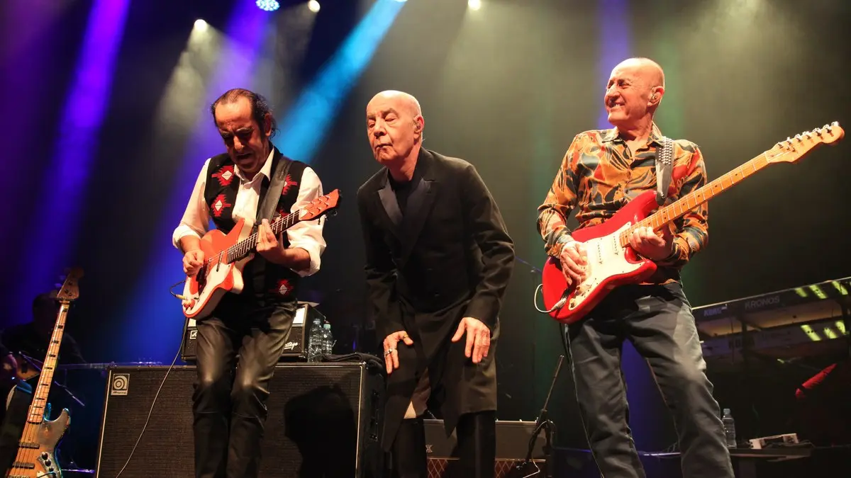MFÖ'nün 2018 konserinde mor ve mavi sahne ışıkları altında gitarlı Mazhar Alanson, ortada Özkan Uğur ve kırmızı elektro gitarıyla Fuat Güner