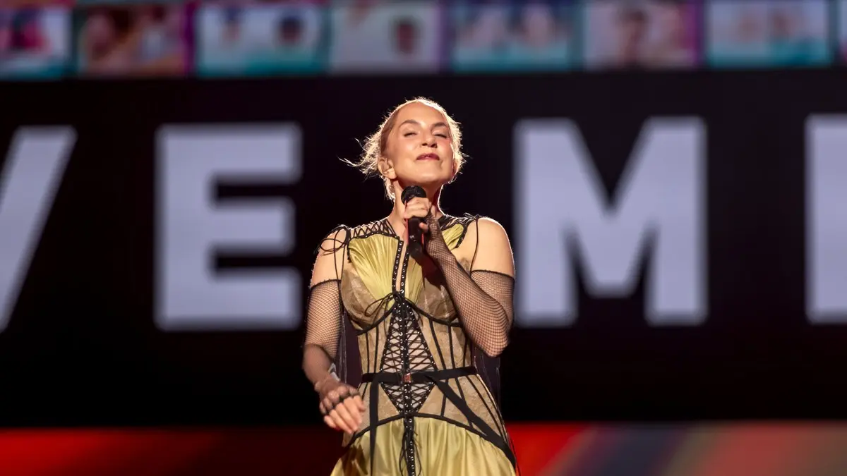 Eurovision 2024 sahnesinde dev harflerin önünde altın rengi elbisesiyle mikrofonu iki eliyle tutarak şarkı söyleyen Sertab Erener