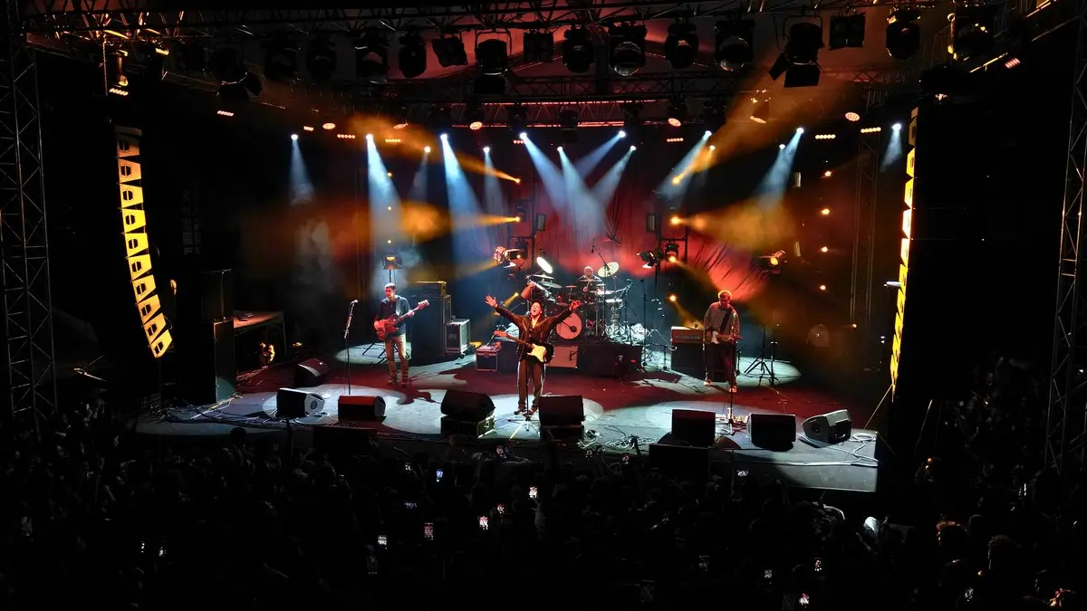 Duman'ın Üsküdar Amerikan Lisesi MayDay festivalindeki konserinde turuncu ve mavi ışık hüzmeleri altında sahnede kollarını açan Kaan Tangöze ve grup üyeleri; önde kalabalık seyirci