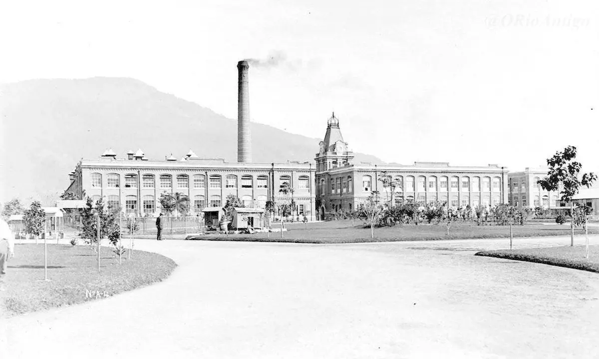 1908 yılında Bangu’daki dokuma fabrikası; uzun bacası tüten büyük fabrika binası, önünde geniş bir yol ve ağaçlar, arkada dağlar; siyah beyaz fotoğraf