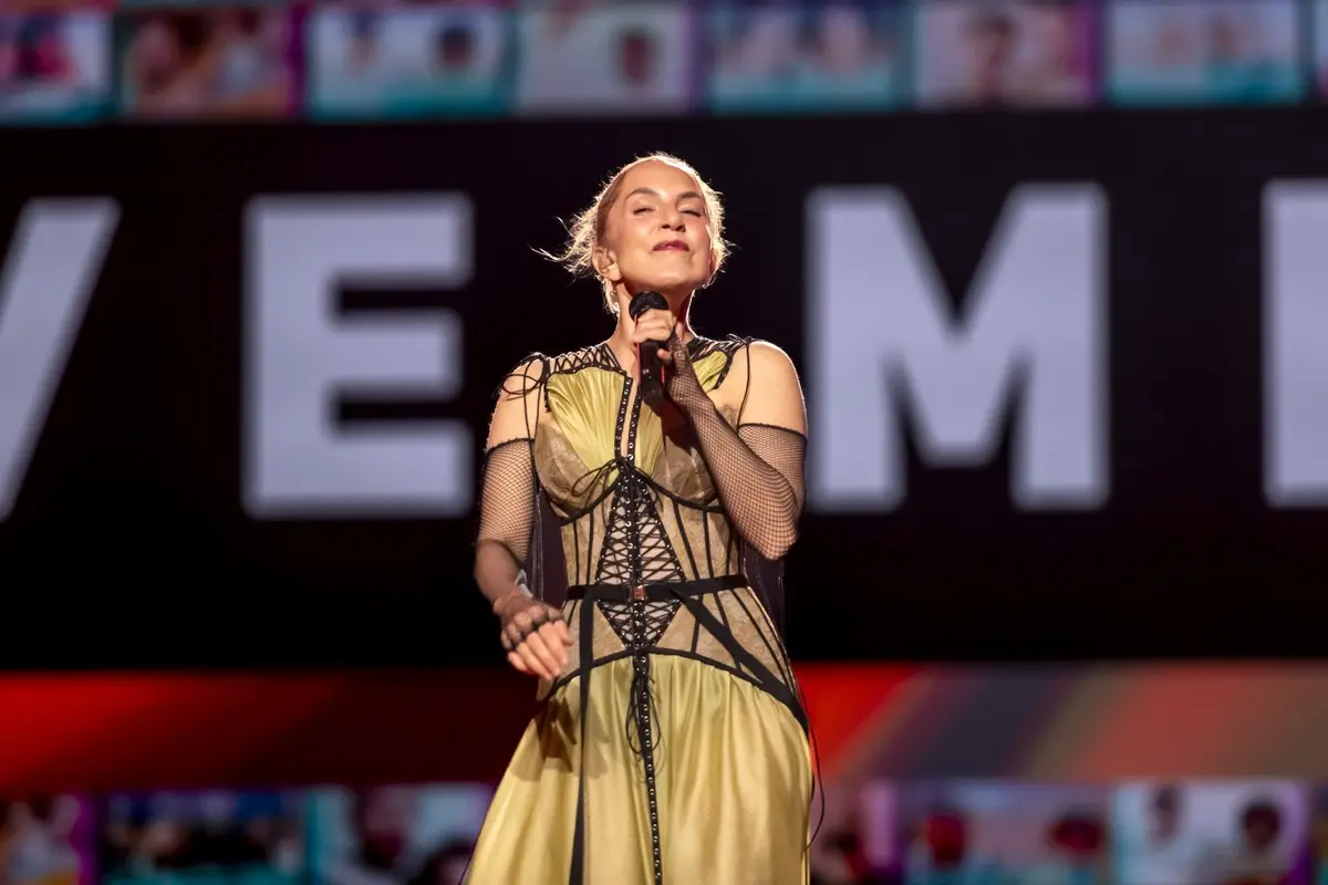 Sertab Erener, 2024’te Malmö’deki Eurovision sahnesinde sarı ve siyah dantelli kostümüyle gözleri kapalı şarkı söylerken; arkada dev ekranda büyük beyaz harfler