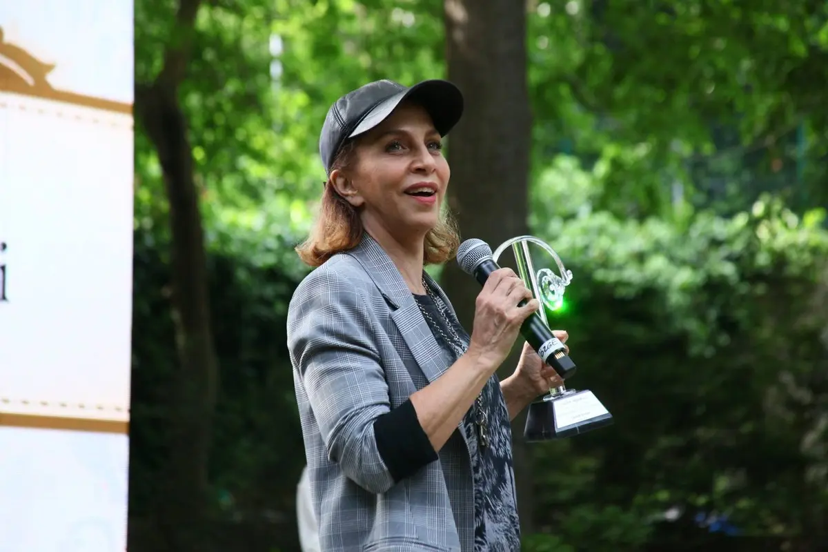 Sertab Erener’in 2018’deki 15. Radyo Boğaziçi Müzik Ödülleri’nde şapkası ve gri ceketiyle, elinde ödülü ve mikrofonla konuşurken çekilmiş fotoğrafı