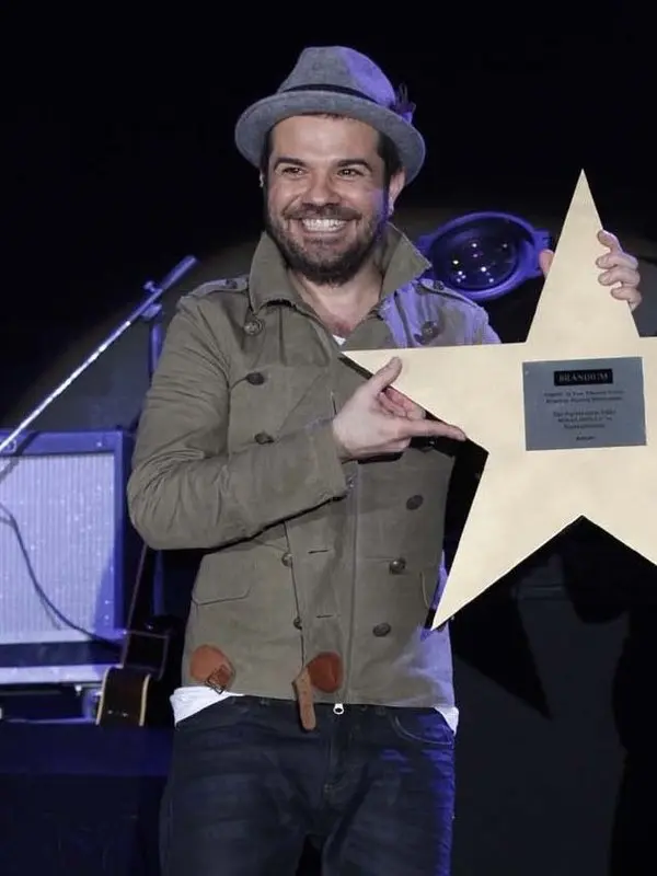 Kenan Doğulu’nun 2013’teki bir konserde şapkası ve haki ceketiyle, elinde yıldız biçimli bir plaketle gülümsediği fotoğraf