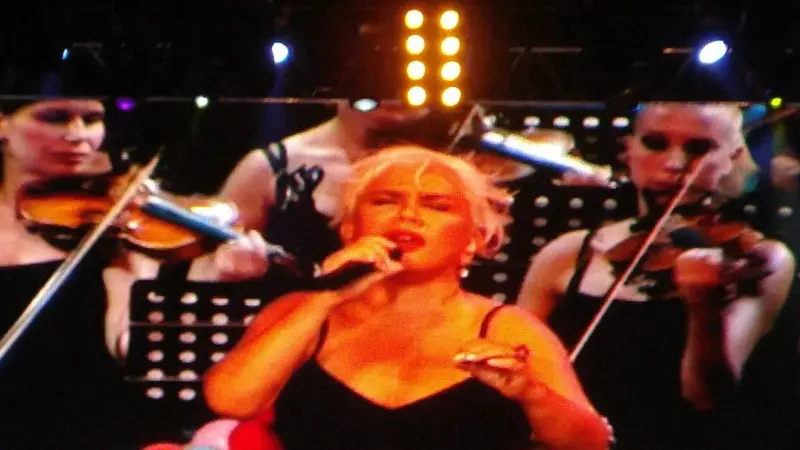Sezen Aksu’nun 2011’deki Harbiye Cemil Topuzlu Açıkhava Tiyatrosu konserinde dev ekrana yansıyan görüntüsü; siyah elbiseli, sarı saçlı Sezen Aksu elinde mikrofonla şarkı söylerken arkasında keman çalan müzisyenler