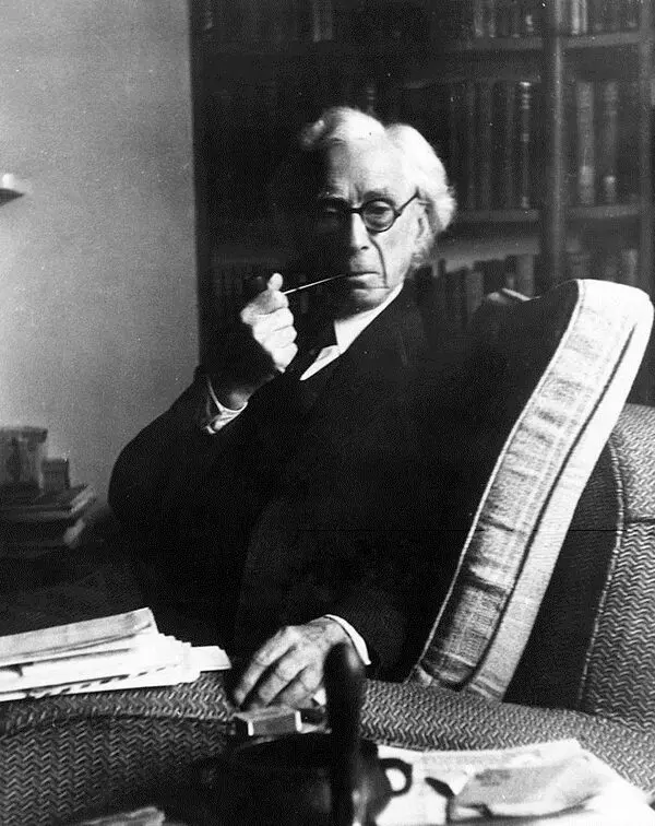 Gözlüklü ve beyaz saçlı Bertrand Russell'ın kitaplığın önündeki bir koltukta oturup sağ elinde ağzına götürdüğü piposuyla kameraya baktığı siyah-beyaz fotoğrafı