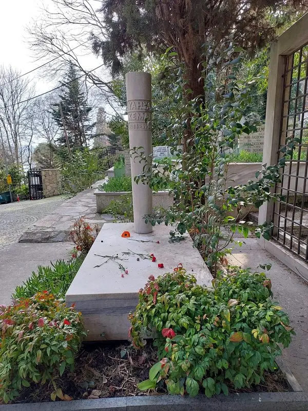 İstanbul Aşiyan Mezarlığı’nda Yahya Kemal Beyatlı’nın beyaz mermer mezarı; mezarın etrafında kırmızı çiçekler ve yeşil bitkiler, arkada ağaçlar