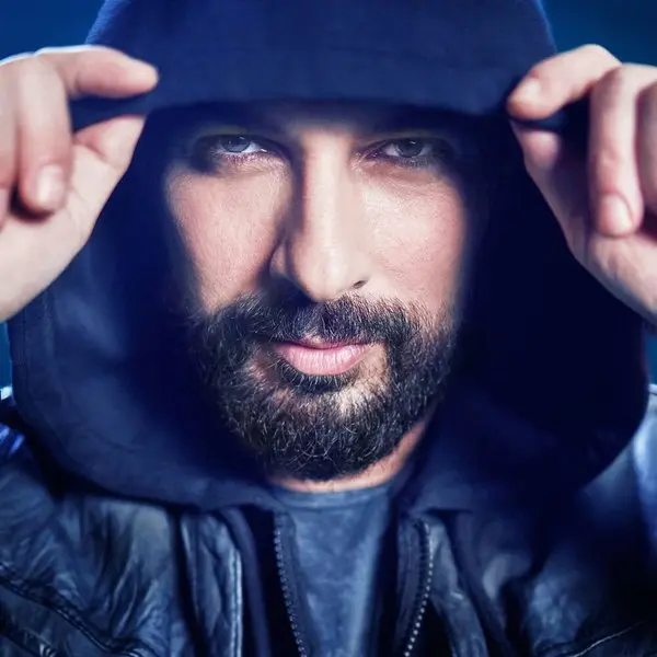 Tarkan’ın Geççek single kapağı; başına kapüşon geçirmiş, iki eliyle kapüşonu tutan sakallı Tarkan’ın koyu tonlu yakın portresi