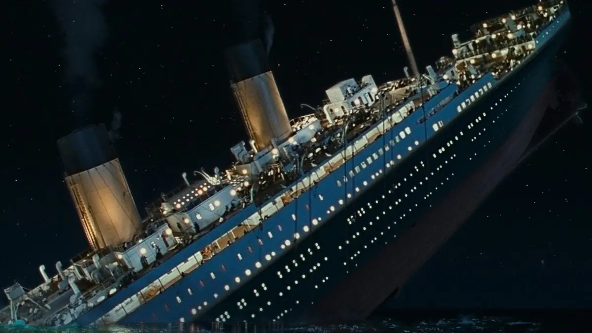 Titanic filminden sahne: gece karanlığında baş tarafı suya gömülmüş, ışıkları hâlâ yanan dört bacalı gemi