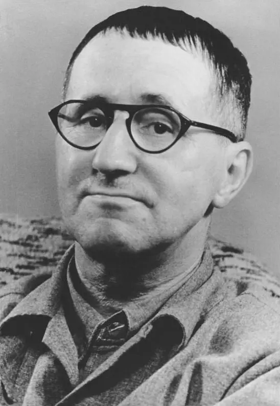 Kısa kesilmiş saçları ve yuvarlak çerçeveli gözlüğüyle hafifçe gülümseyen Bertolt Brecht'in yakın plan siyah-beyaz portresi