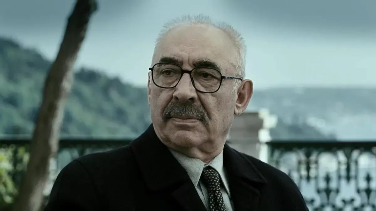 Av Mevsimi filminden, gözlüklü, takım elbiseli yaşlı bir adamın yakın planı