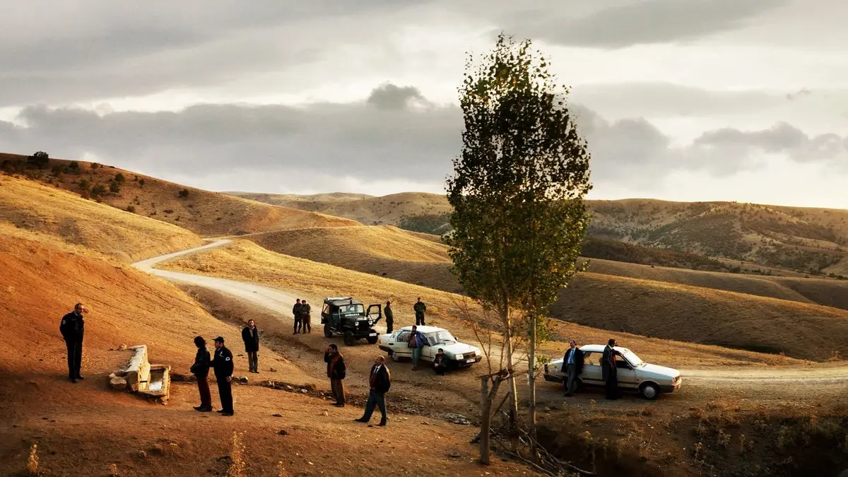 Bir Zamanlar Anadolu'da filminden, bozkırda yalnız bir ağacın yanında duran arabalar ve bir grup adam