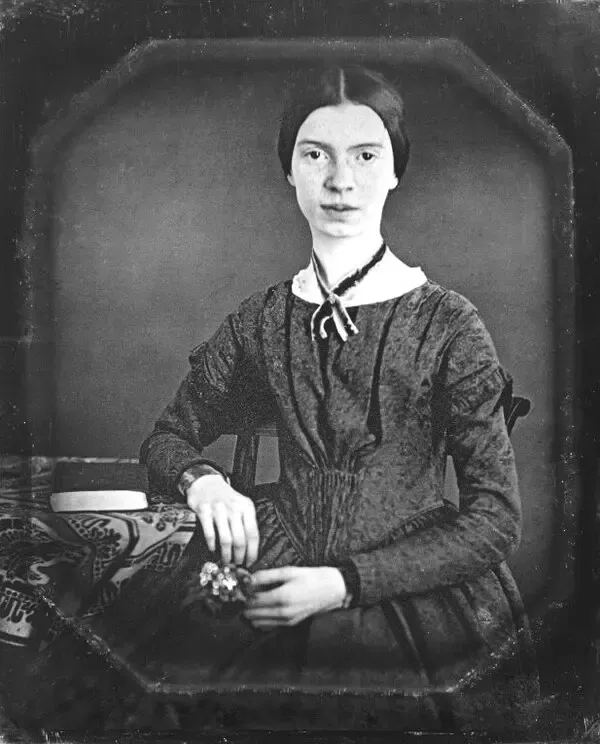 Genç Emily Dickinson'ın koyu elbisesi ve boynundaki kurdeleyle bir masanın yanında oturup elinde küçük bir çiçek tuttuğu dagerotip portresi