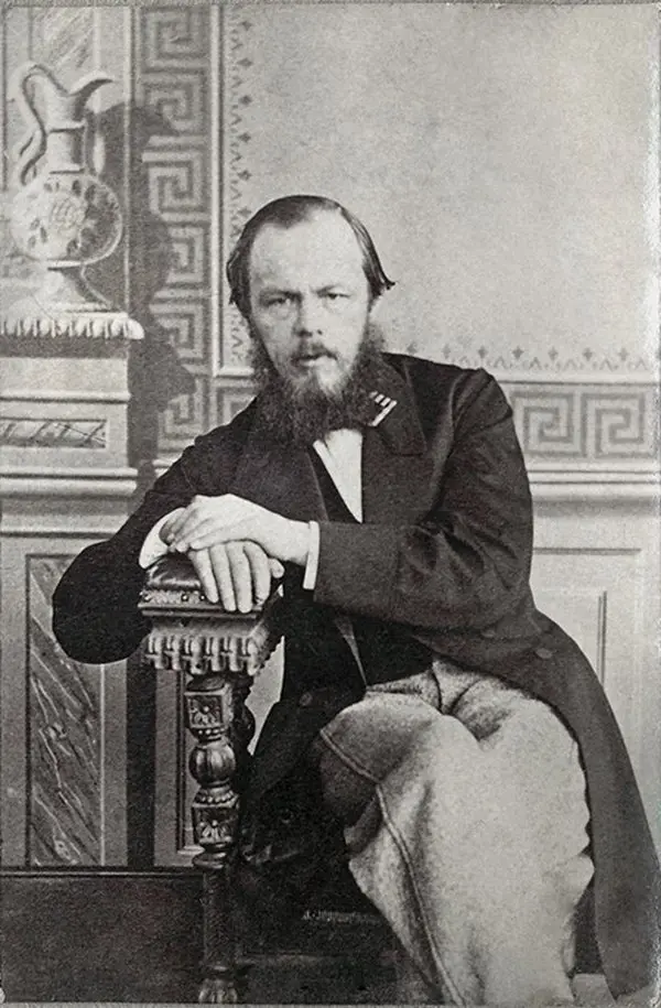 1863 tarihli siyah beyaz stüdyo fotoğrafında uzun redingotlu, sakallı Fyodor Dostoyevski, kollarını oymalı bir sandalyenin arkalığına dayamış, arkada desenli duvar ve vazo