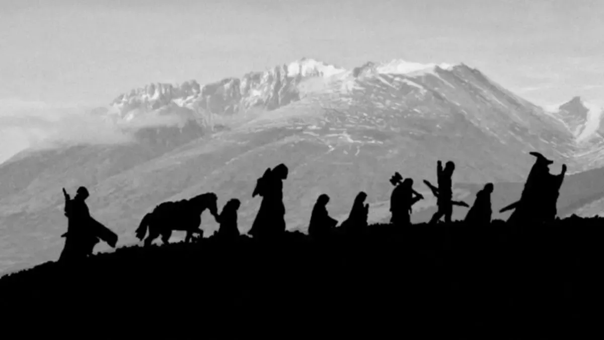 Karlı dağların önünde bir sırt boyunca tek sıra yürüyen Yüzük Kardeşliği üyelerinin siyah siluetleri, aralarında bir midilli ve asasıyla Gandalf