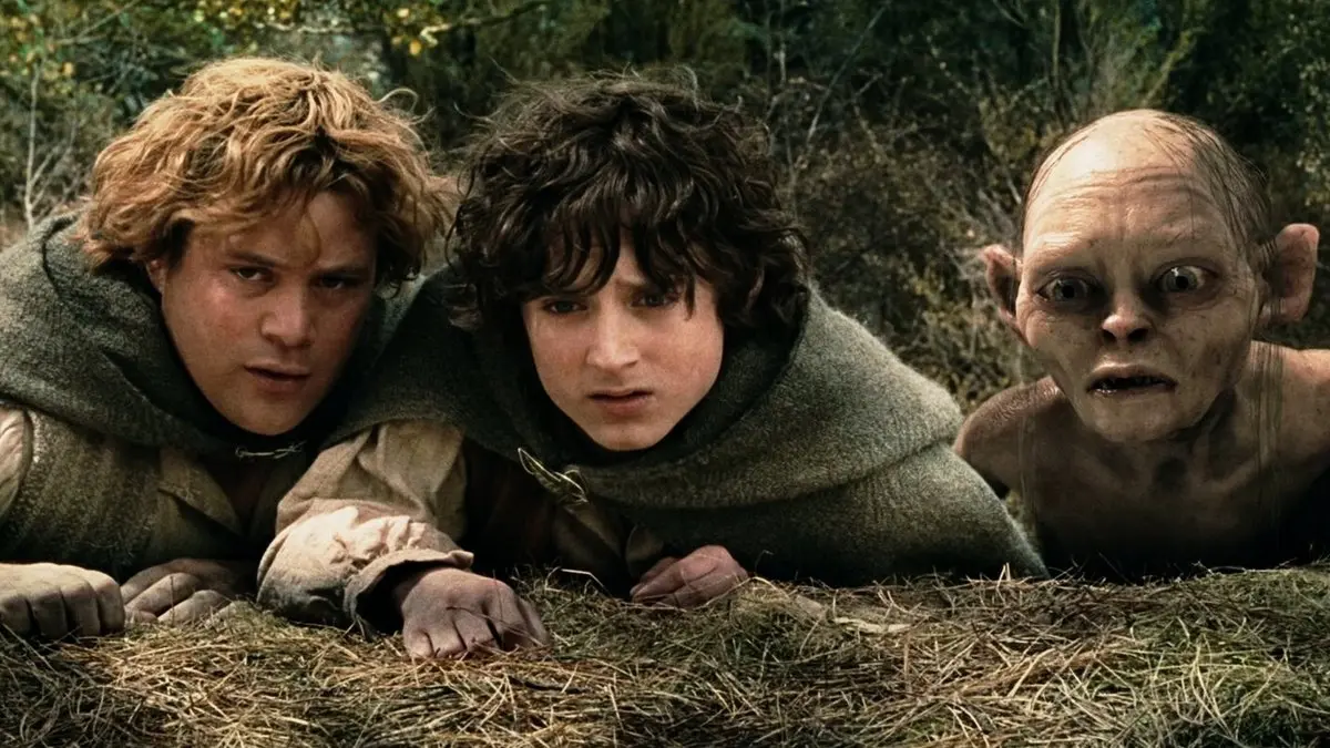 İki Kule filminden sahne: çimenlerin arasında yere yatıp saklanan Sam ve Frodo, yanlarında iri gözleriyle bakan Gollum