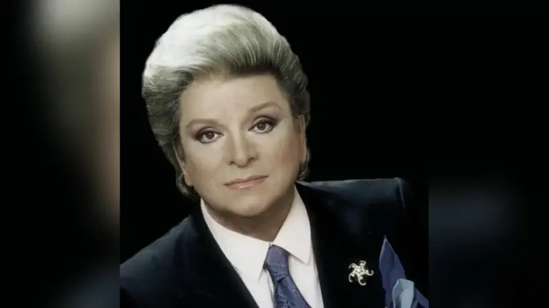 Zeki Müren’in koyu zemin önünde lacivert ceket, kravat ve broşla çekilmiş portre fotoğrafı